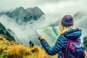 Eine junge Frau in Berglandschaft schaut auf eine Landkarte als Symbol für den Themen-Navigator