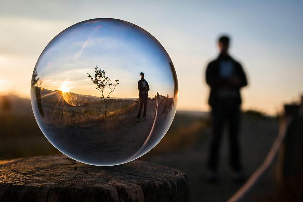 Mensch spiegelt sich in einer Glaskugel als Symbol für existenzielle Themen